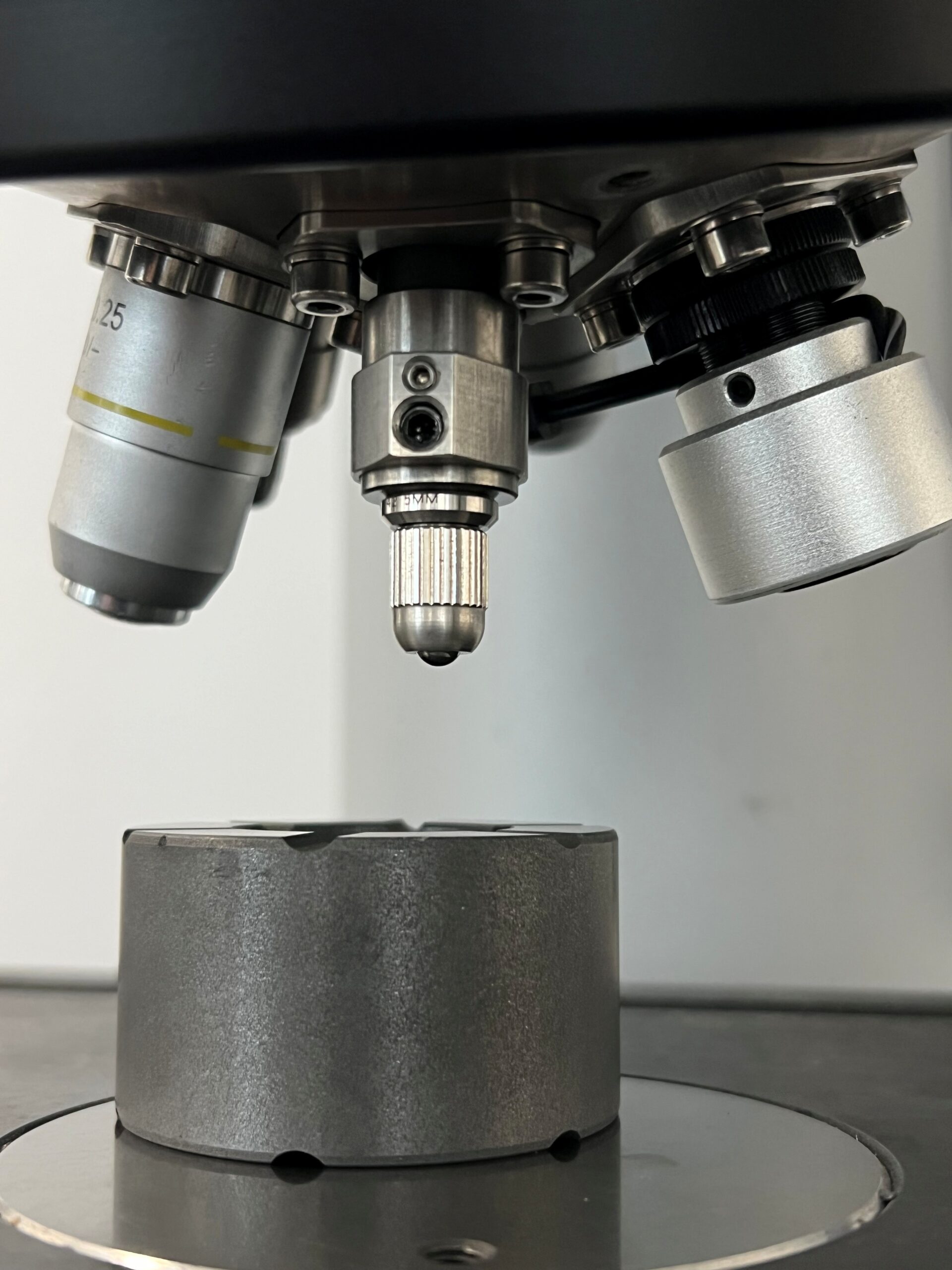 Kohlenstoffprobe unter dem Härteprüfer: Die spröde, poröse Struktur erfordert das speziell abgestimmte Verfahren nach DIN 51917. Kohlenstoffprobe unter dem Härteprüfer mit Eindringkörper im Detail